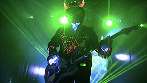 Simon Posford playing guitar with top hat and horns in green light silhouette