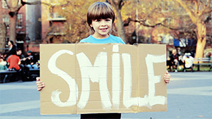 young girl holding inspirational sign in park saying smile