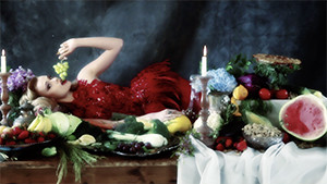 fashion model in studio wearing red dress laying on table surrounded by fruit