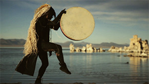 shaman with drum dancing by water