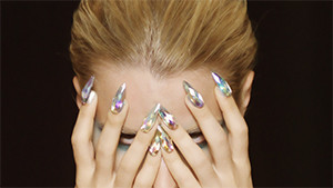 Fashion model in studio with colorful nails looking through hands on face