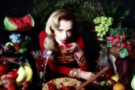 fashion model in studio at table eating pie with hands surrounded by fruits
