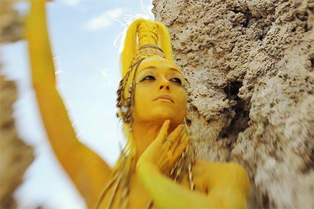 Amy Secada as Oxum in yellow body paint sitting on rock